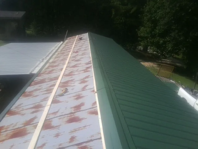 Old rusted panels beside newly installed green metal roofing — Wind Damage Roof Repair by Roofing Brothers in Webster City