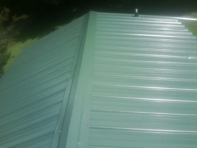 New green metal panels meeting at the ridge of a roof — Flat Roof Repair work by our crew in Webster City