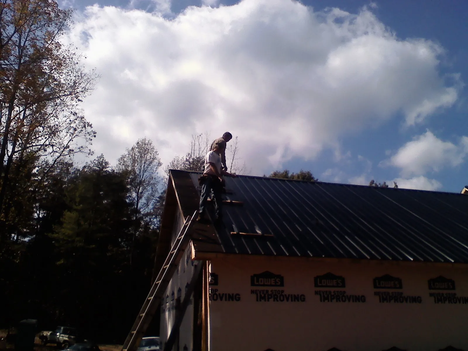 Roofer fastening dark metal panels high against a cloudy sky, from a Roof Inspection job in Webster City