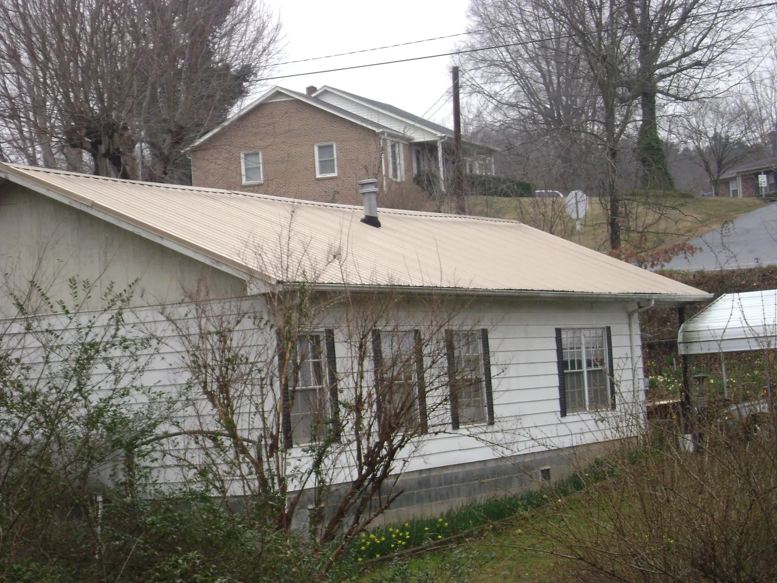 Tan metal roof on a white sided house set into a hillside — Commercial Roofing by Roofing Brothers in Webster City