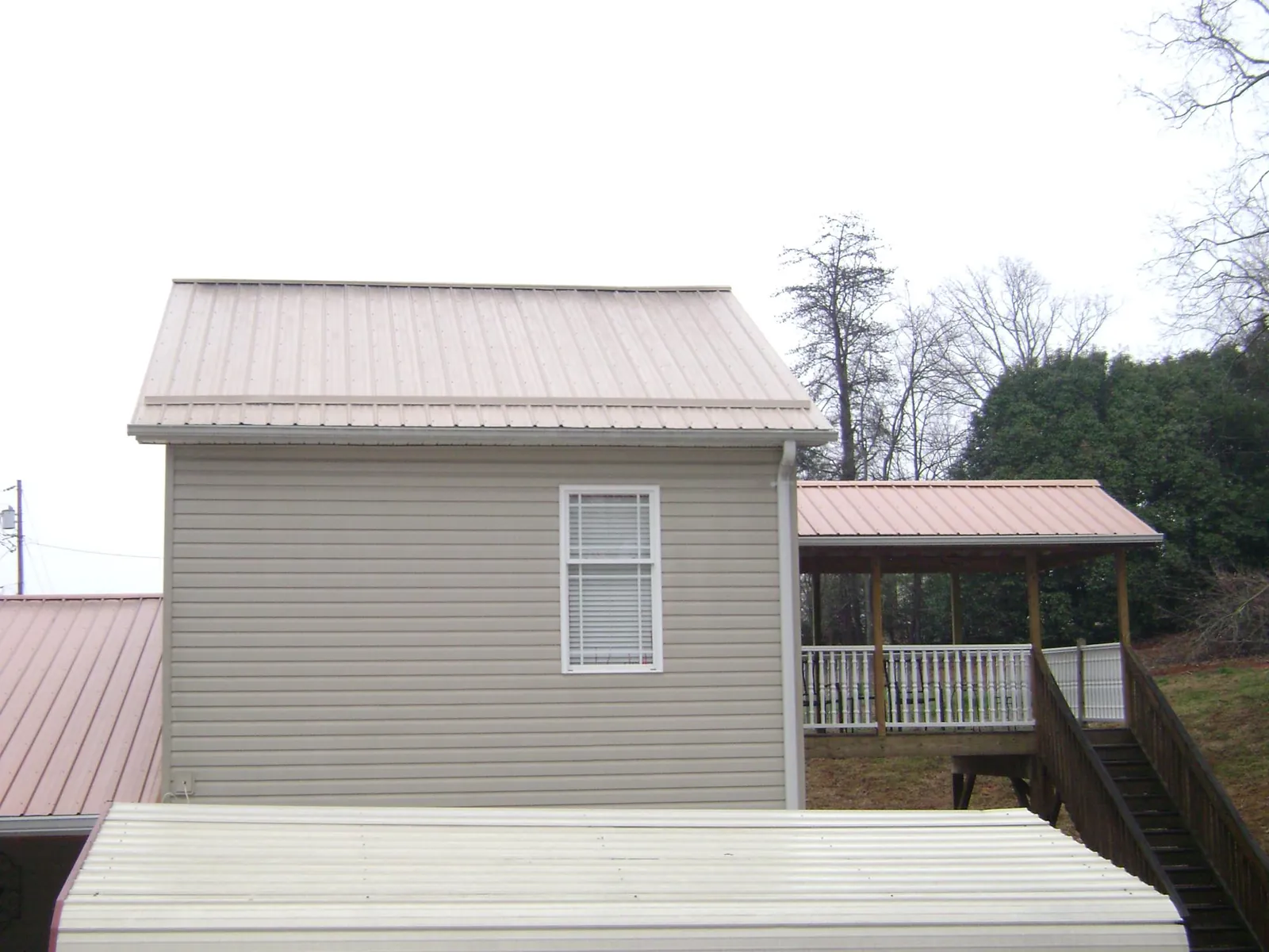 Tan metal roofs on a two story addition and attached porch, from a Roof Replacement job in Webster City